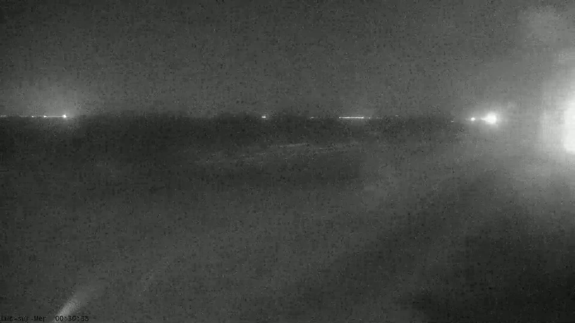 A nighttime, low-visibility scene shows a dark landscape with faint lights in the distance.