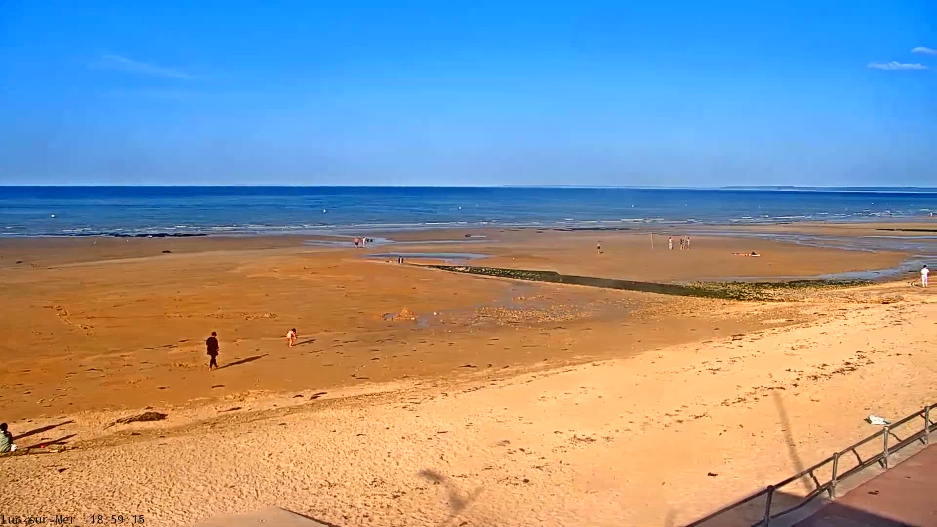 A wide sandy beach stretches to a calm blue ocean under a clear blue sky.