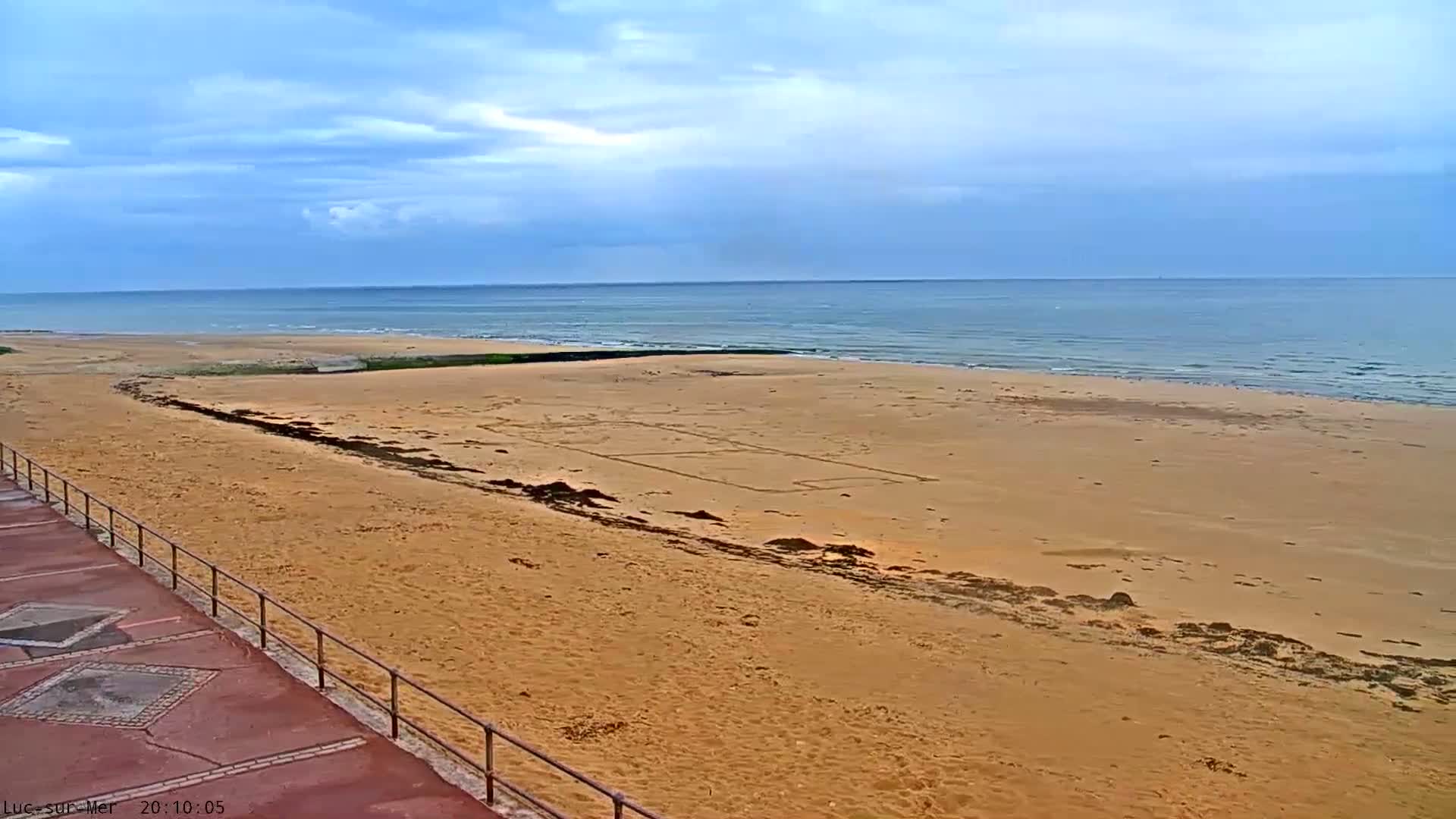 A mostly sunny day shows a wide sandy beach with a large drawing in the sand and a calm ocean in the background.