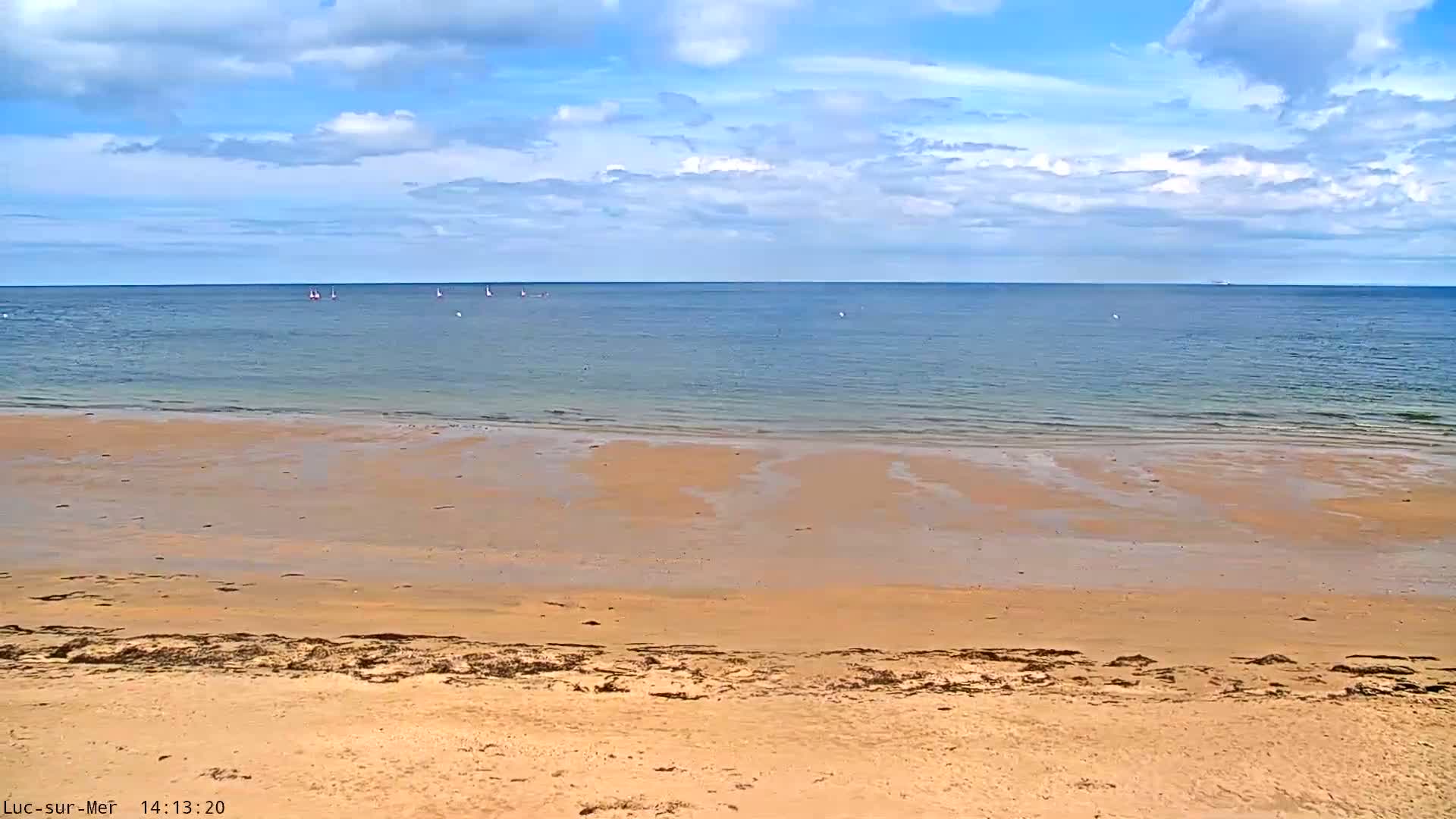 A sandy beach slopes down to a calm, light-blue ocean under a partly cloudy sky.