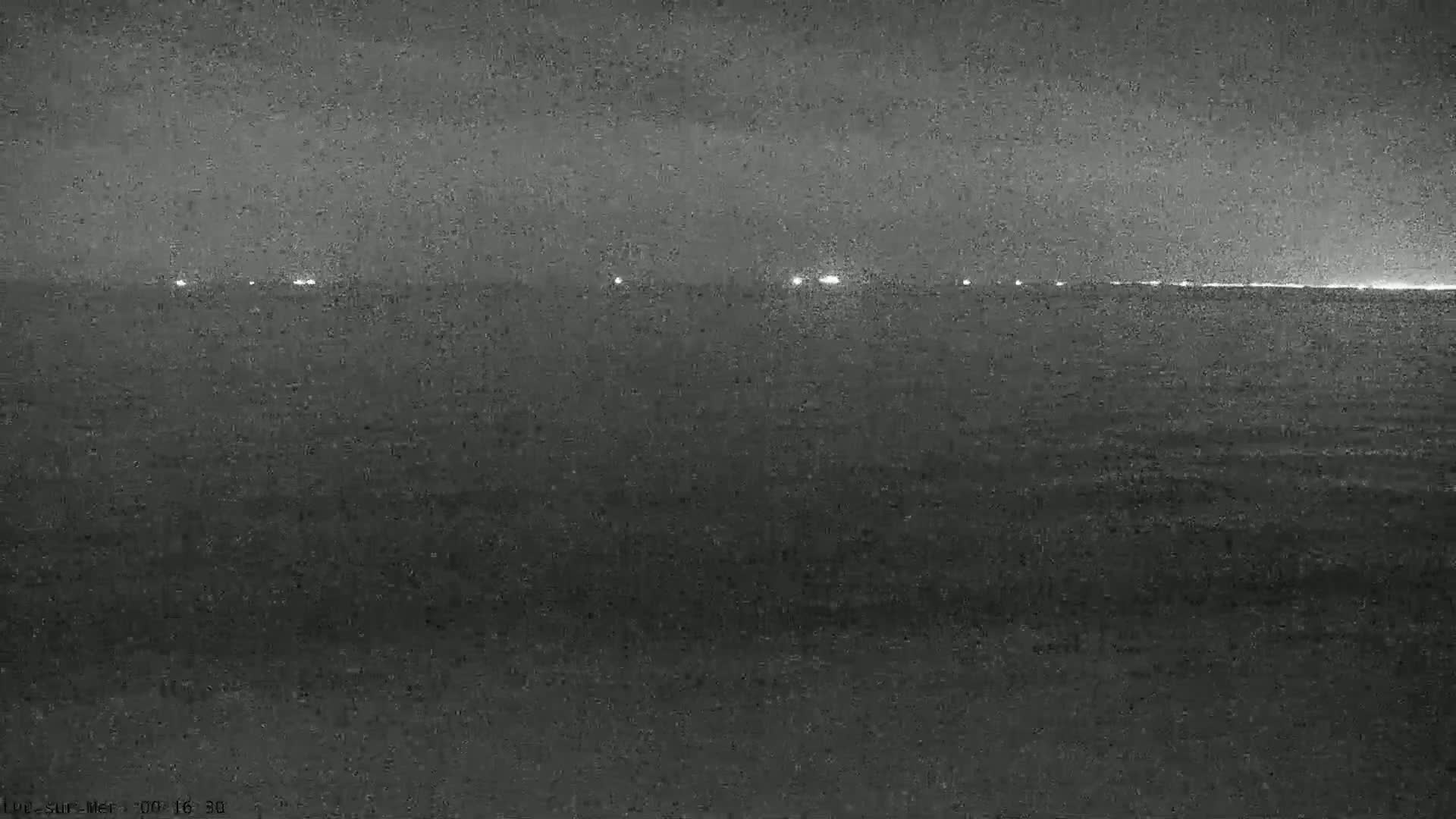 A dark, nighttime view of a calm body of water with faint lights visible on the horizon.