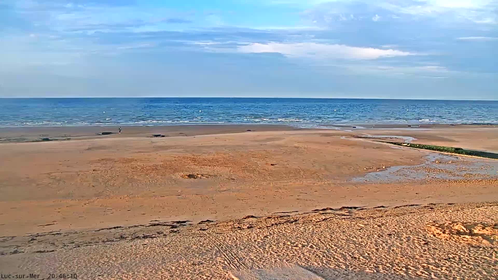 A wide sandy beach stretches to a calm, blue ocean under a mostly clear sky.