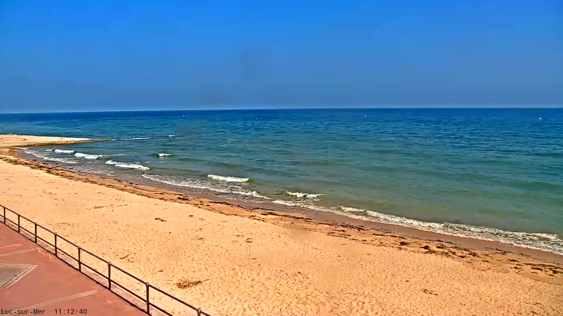 A sandy beach slopes gently down to a calm, teal ocean under a clear blue sky.