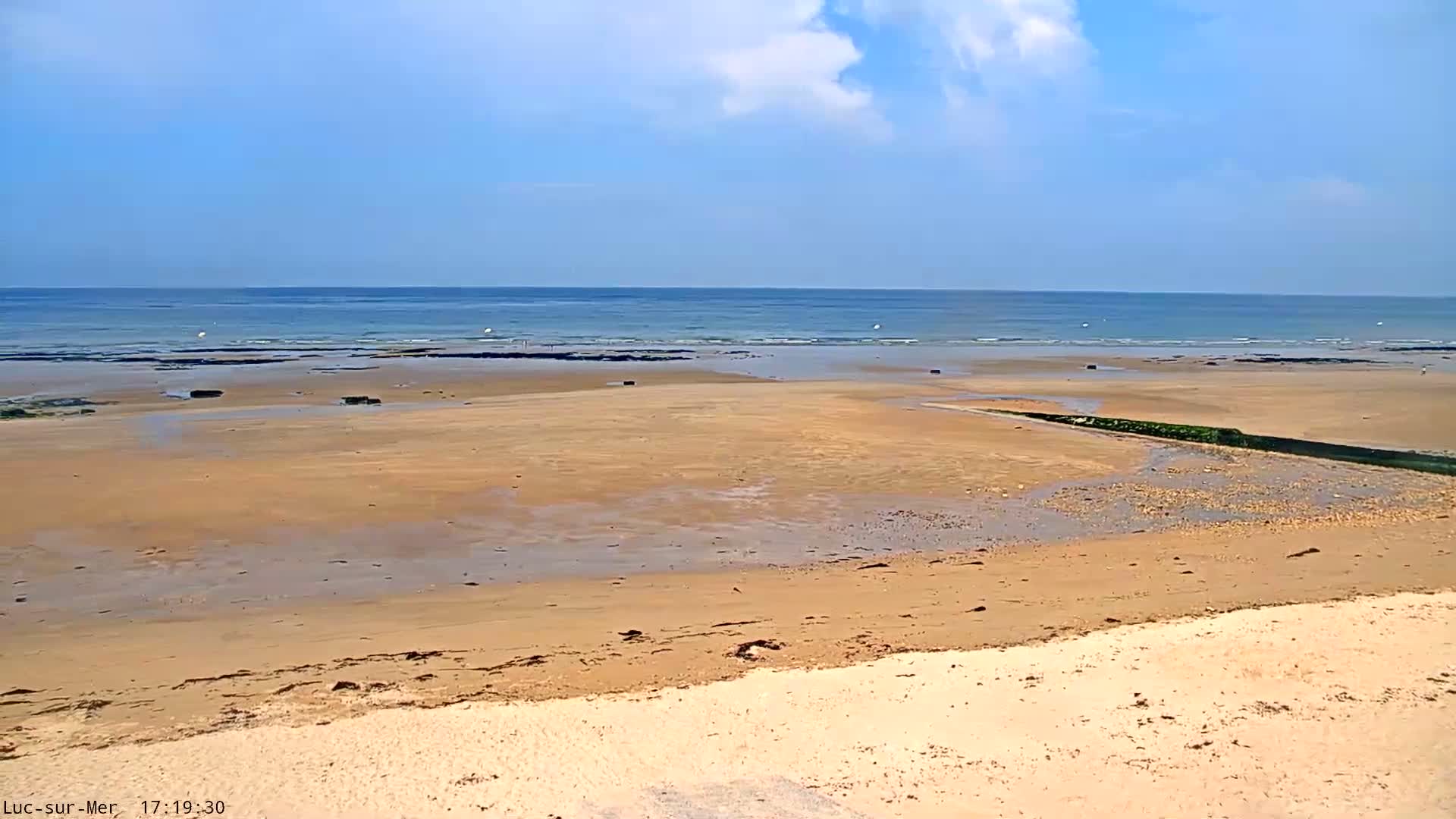 A wide sandy beach stretches to a calm ocean under a mostly clear blue sky.