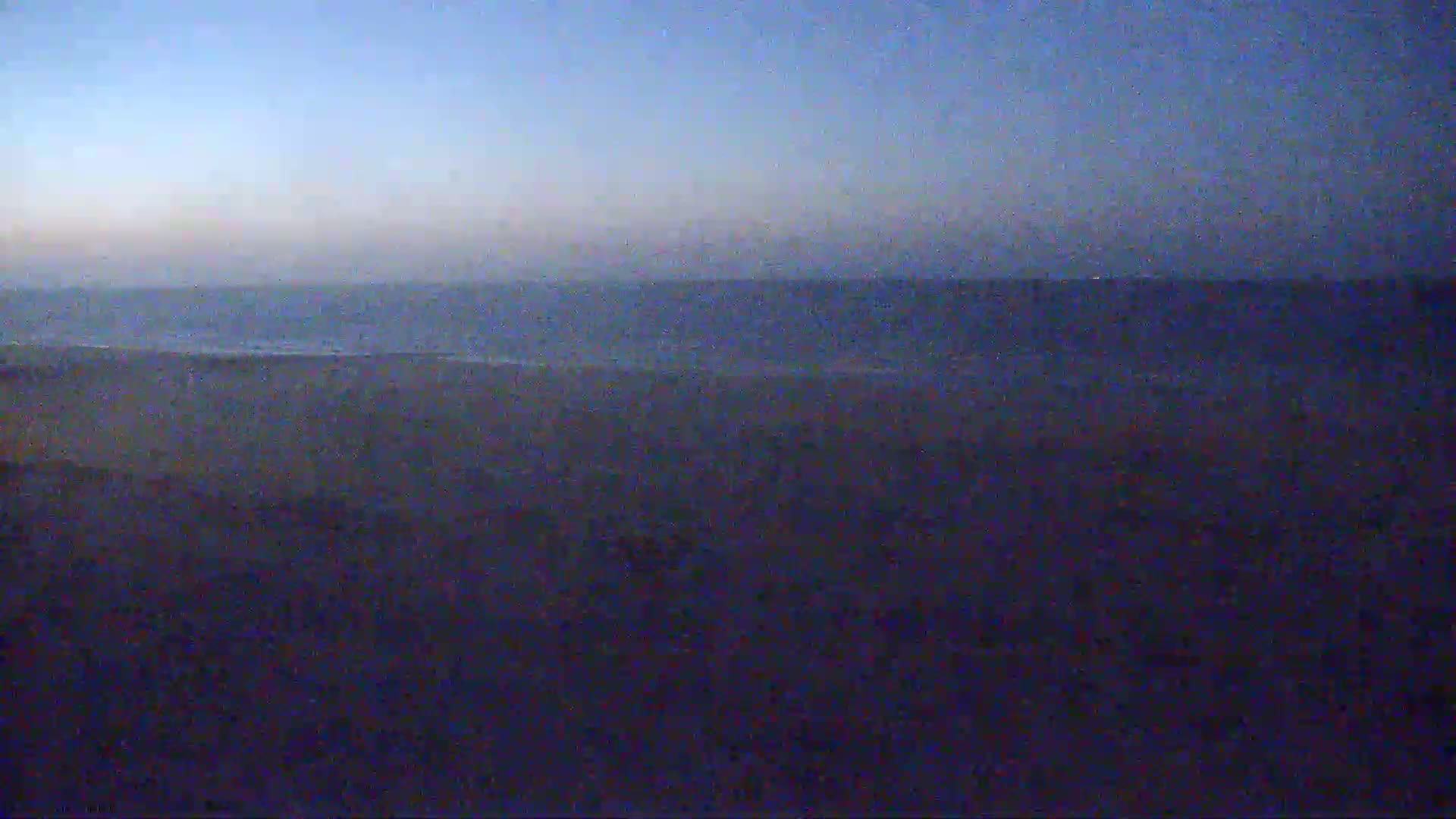 A dark beach and calm ocean are visible under a twilight sky.