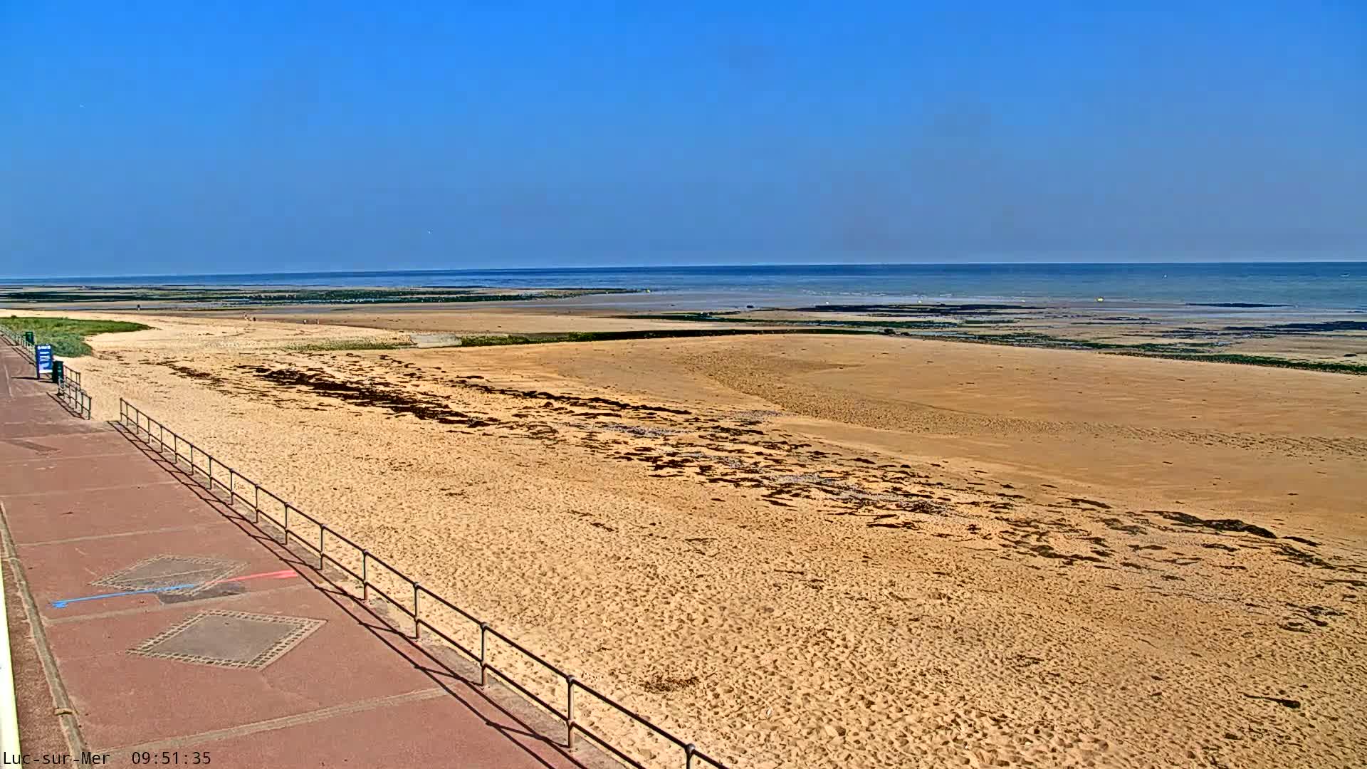 A wide sandy beach stretches to a calm ocean under a clear blue sky.