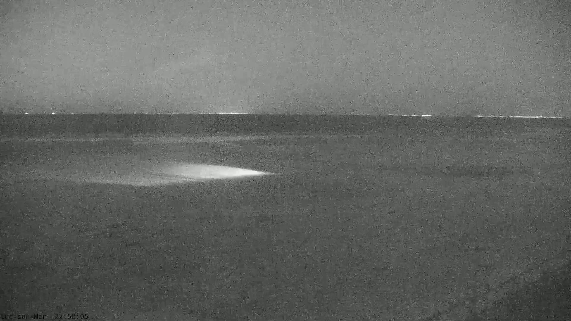 A nighttime grayscale image shows a dark body of water under a dark sky, with a faint light source visible on the water's surface.