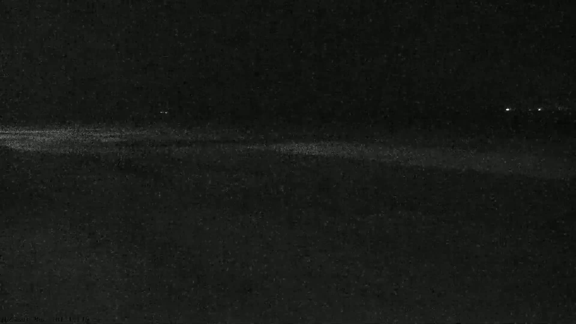 A dark, nighttime scene shows a flat, indistinct expanse with a few faint lights in the distance.