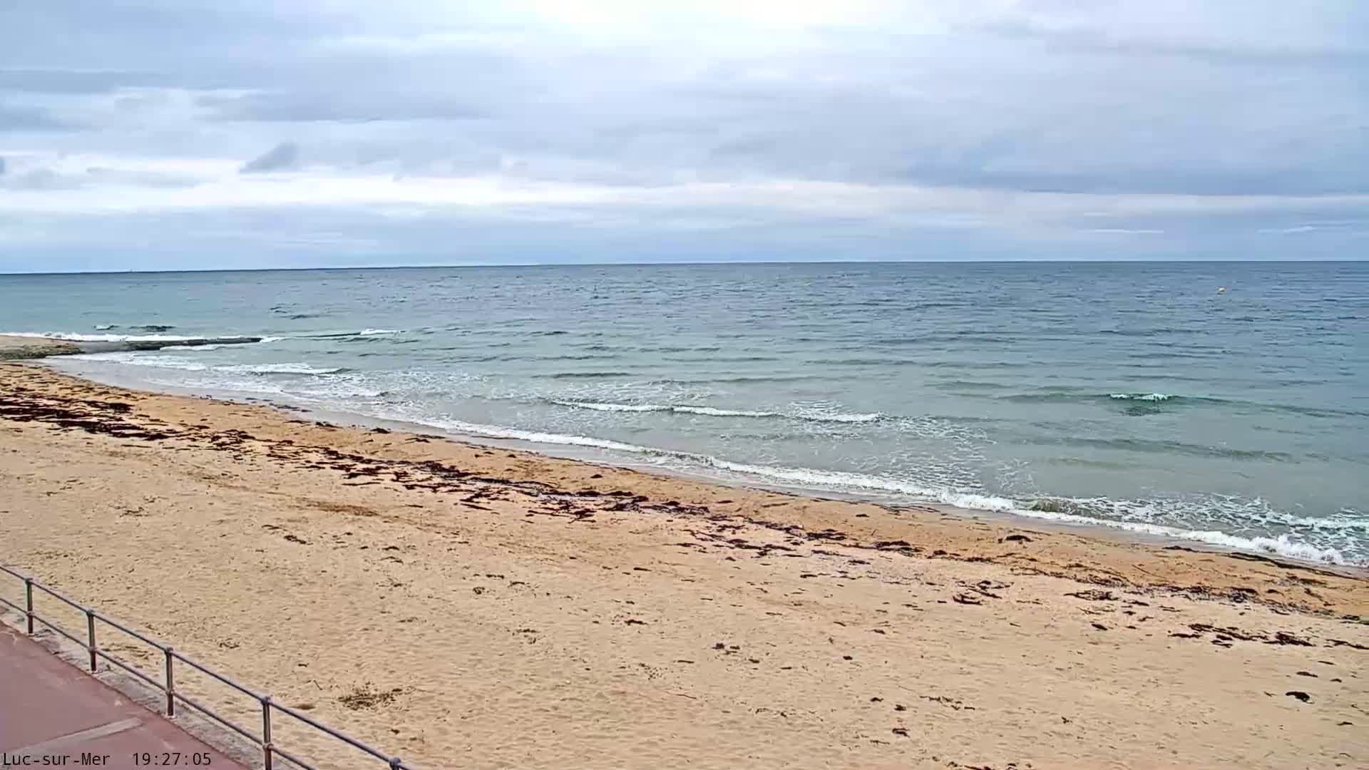 A sandy beach with small waves gently lapping the shore under a cloudy sky.