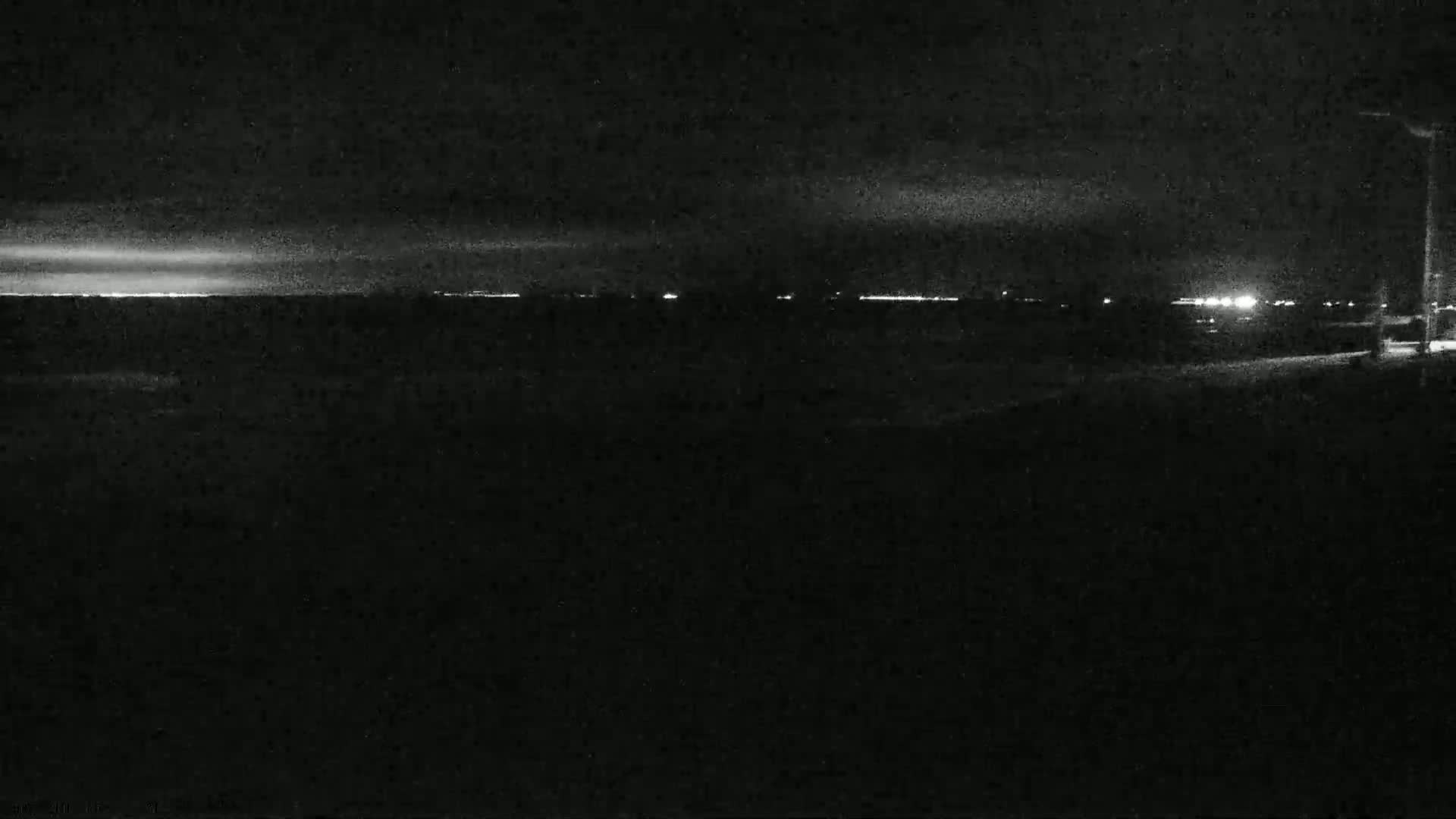 A nighttime, low-light view shows a dark landscape with a faint horizon line illuminated by distant lights.