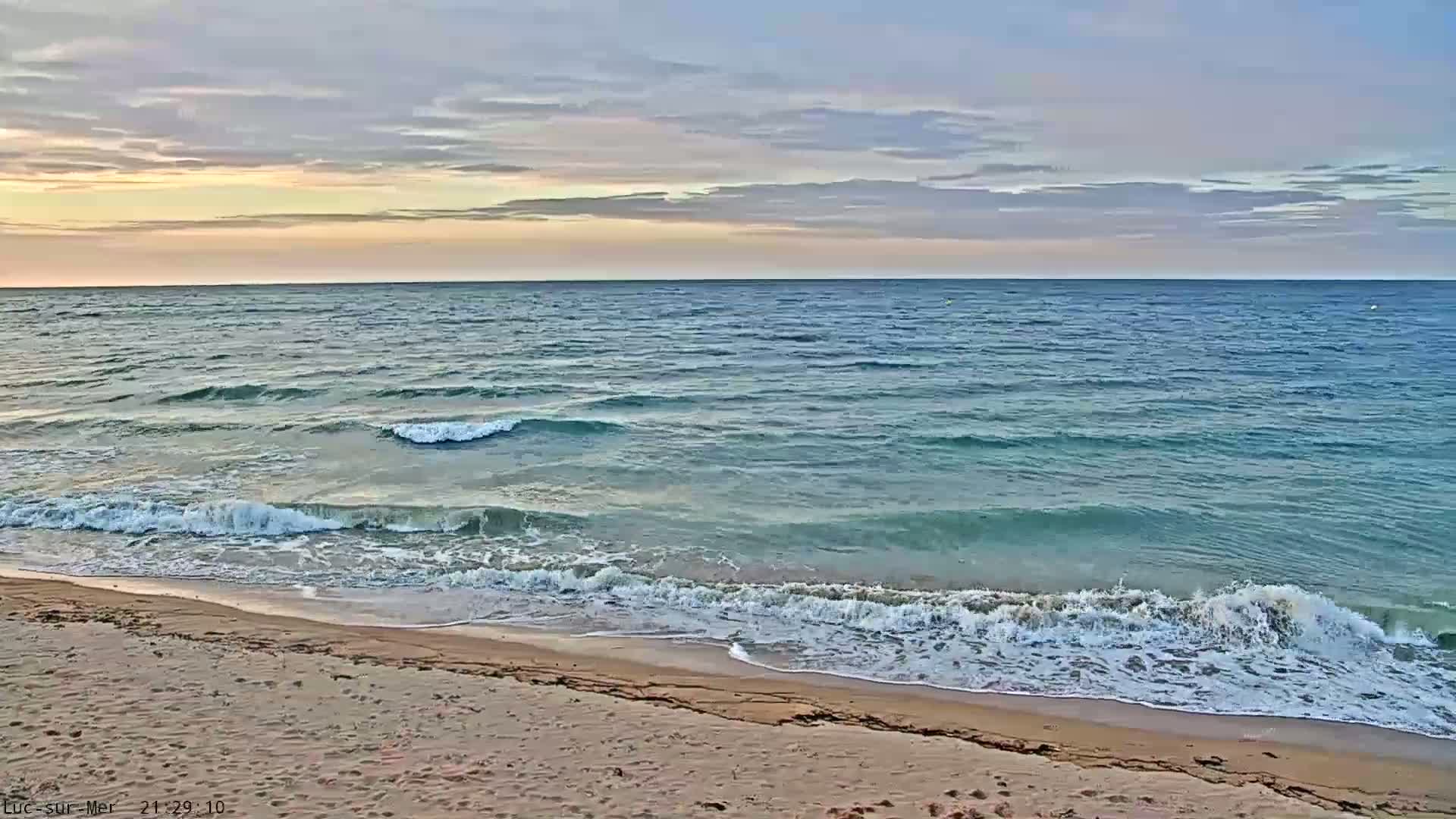 Under a partly cloudy sky, gentle waves lap a sandy beach.