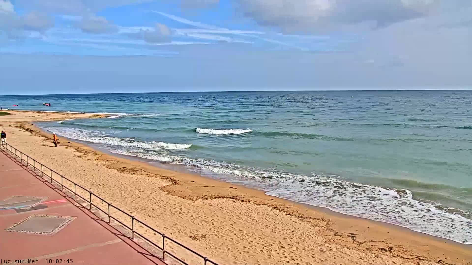 A sandy beach with gently rolling waves under a partly cloudy sky.