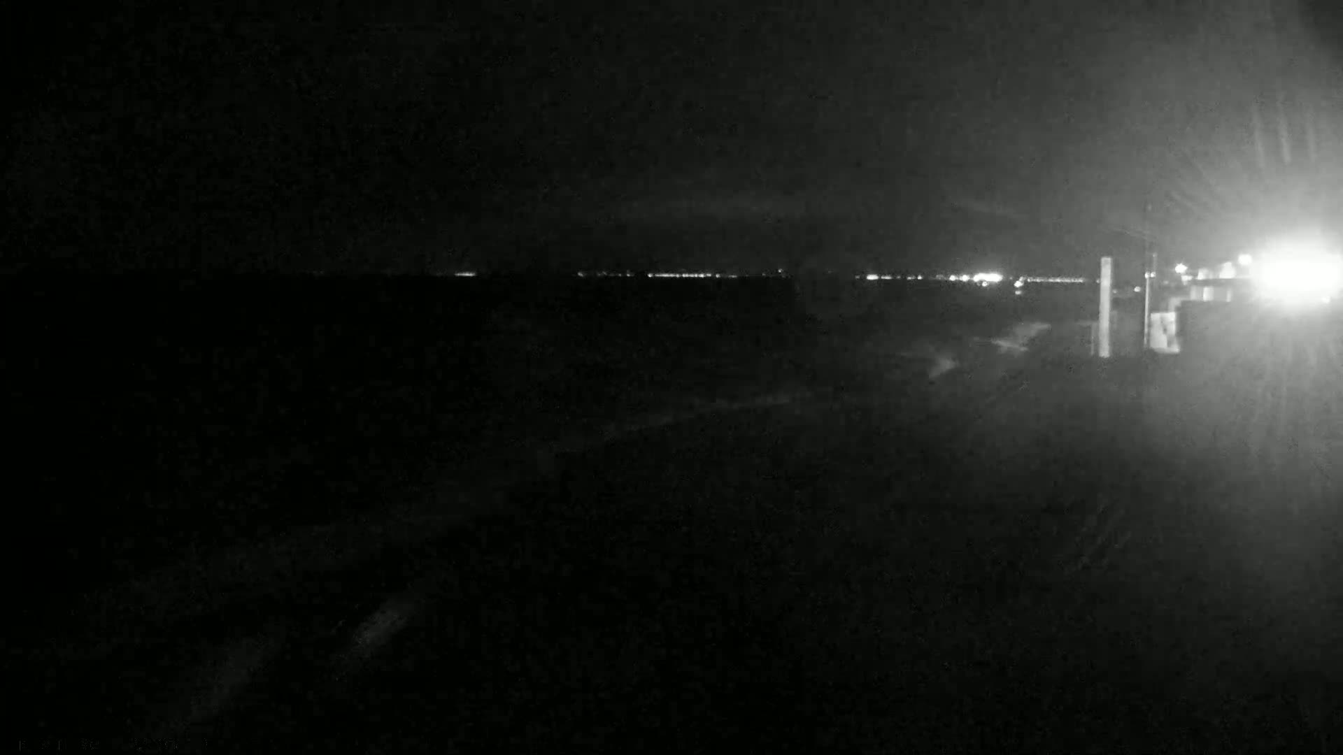 A nighttime, low-light image shows a dark, seemingly empty landscape with a distant line of lights on the horizon.