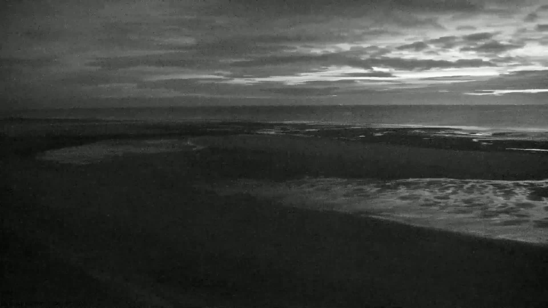 A dark, overcast sky hangs over a beach at night, where gentle waves lap the shore.