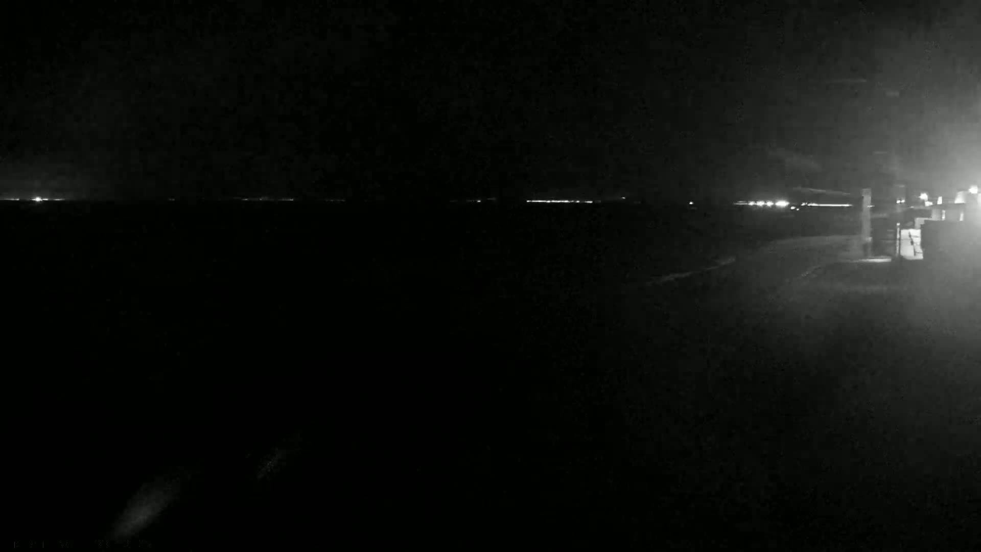 A dark, nighttime scene shows a distant line of lights on the horizon under a mostly clear sky.