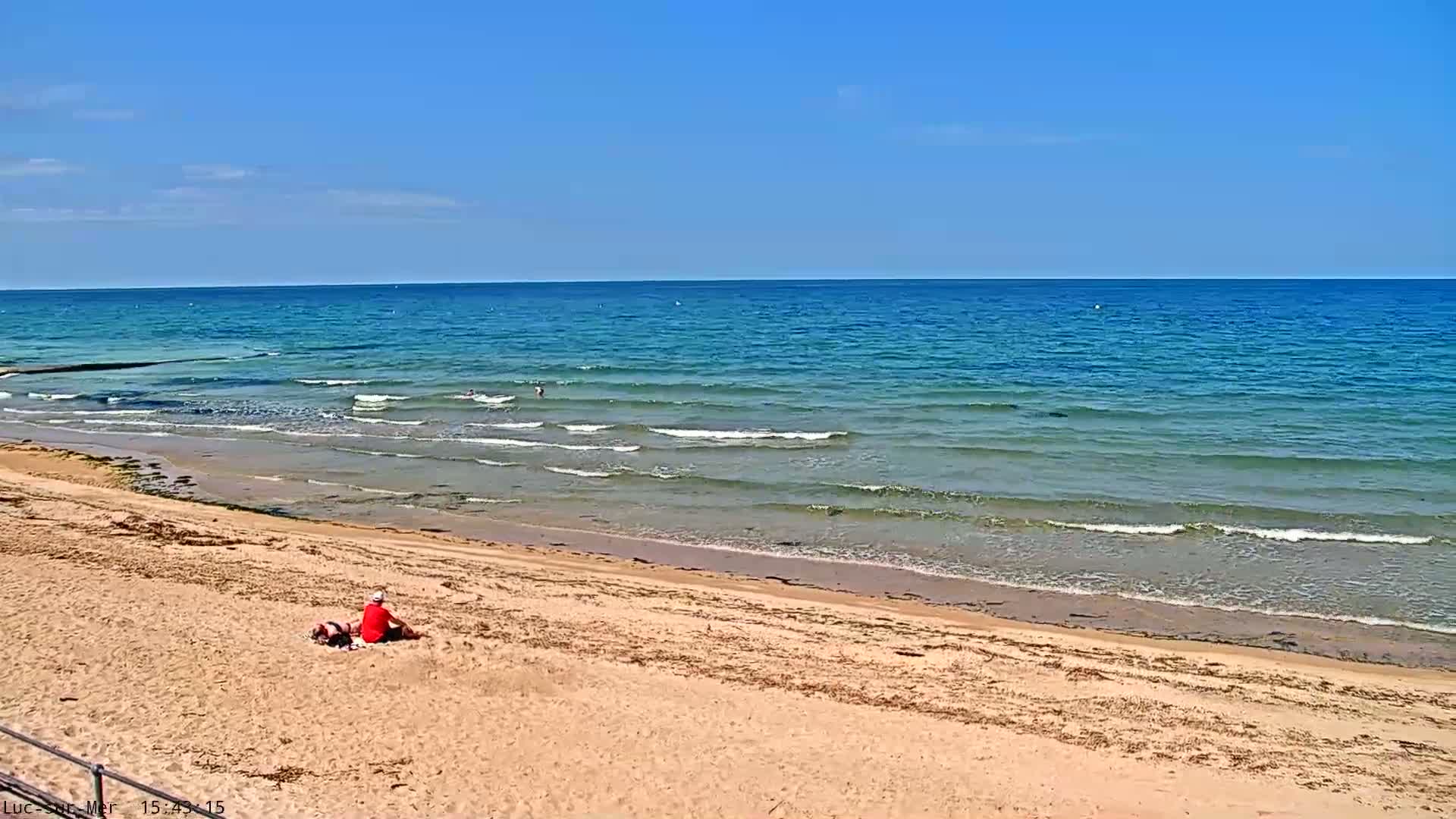 A sandy beach slopes gently down to a calm, turquoise ocean under a clear blue sky.