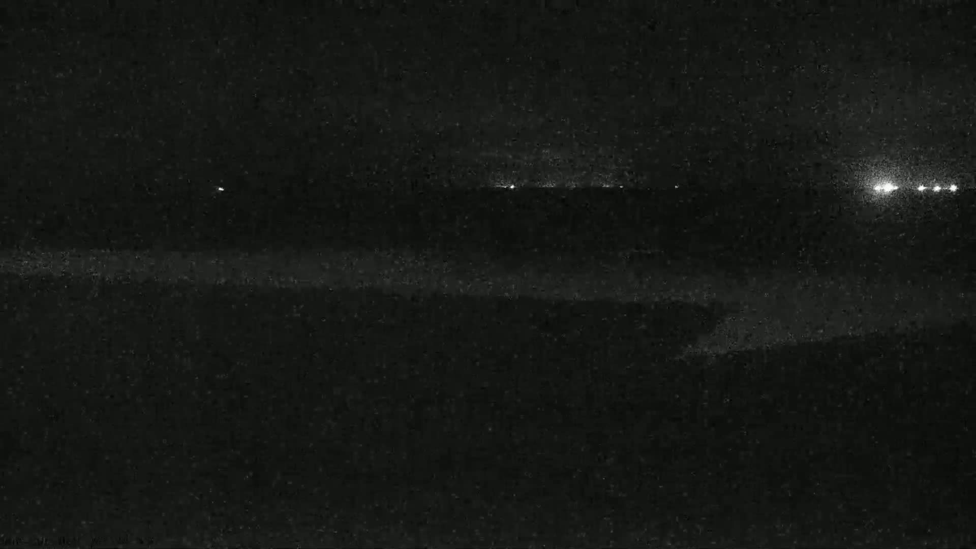 A nighttime, low-light view shows a dark landscape with a few distant lights visible on the horizon.