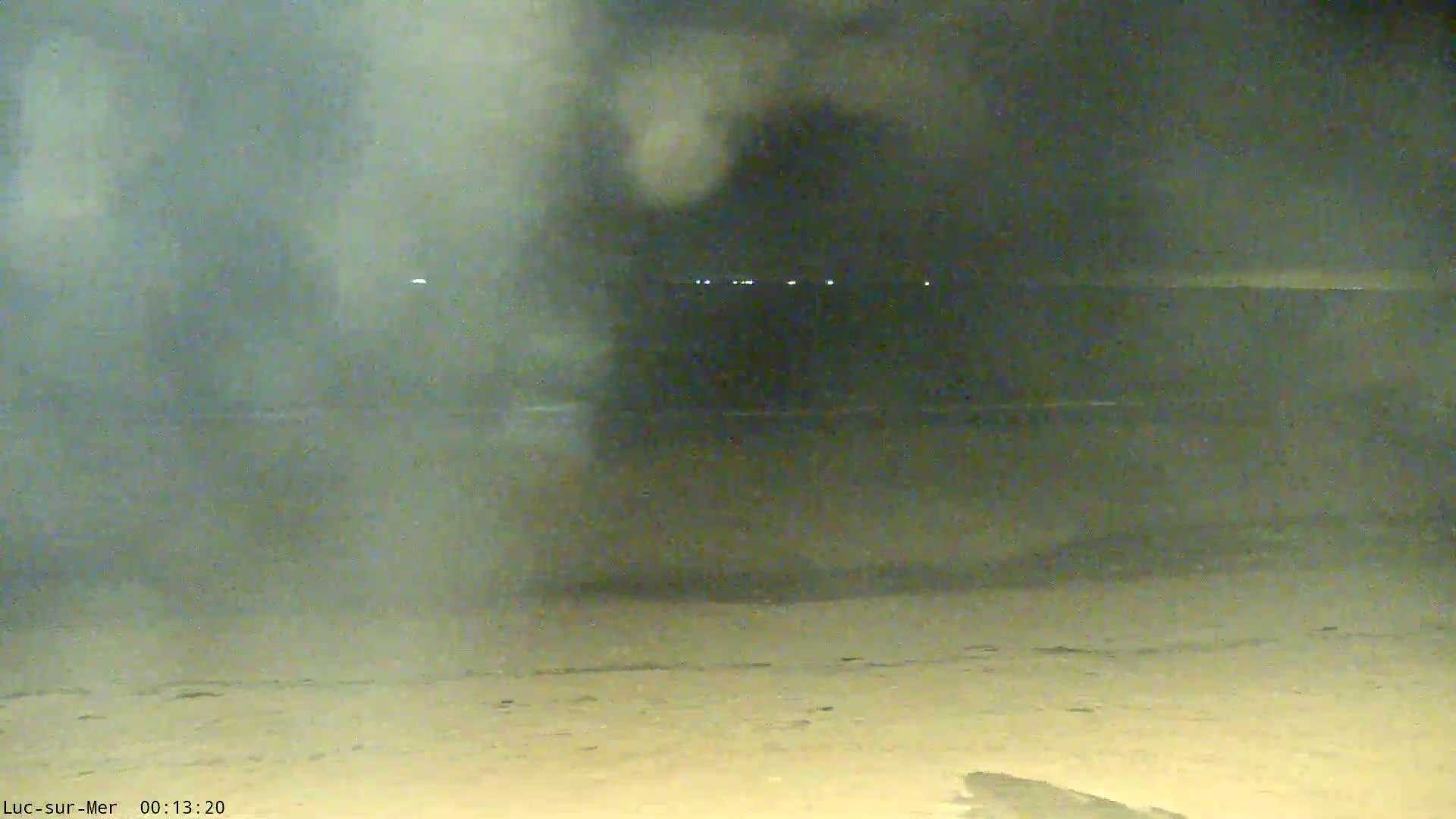A nighttime beach scene is obscured by a hazy, foggy atmosphere, with faint lights visible in the distance.