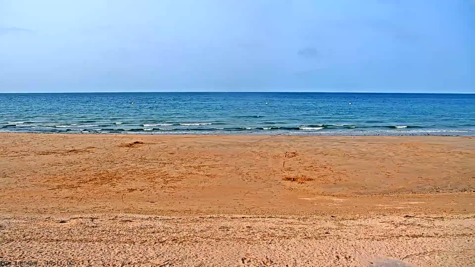 A sandy beach slopes gently down to a calm, blue ocean under a clear sky.