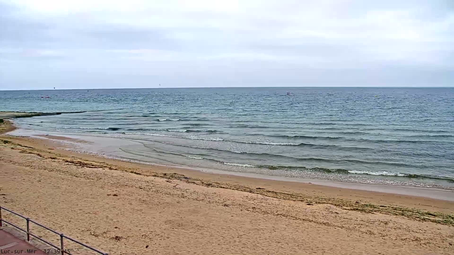 A sandy beach slopes gently down to a calm sea under a cloudy sky.