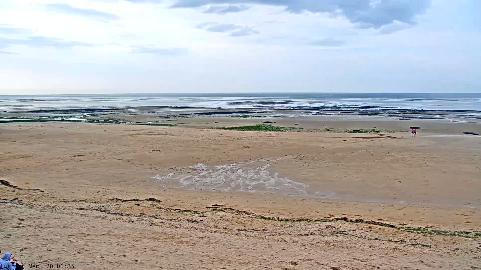 A wide sandy beach stretches toward a calm, gray-toned ocean under a cloudy sky.