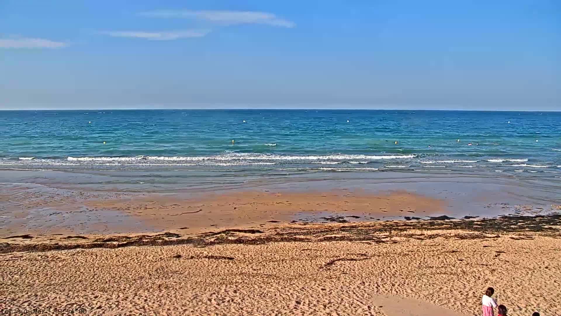 A sandy beach slopes down to a calm, blue ocean under a clear, sunny sky.