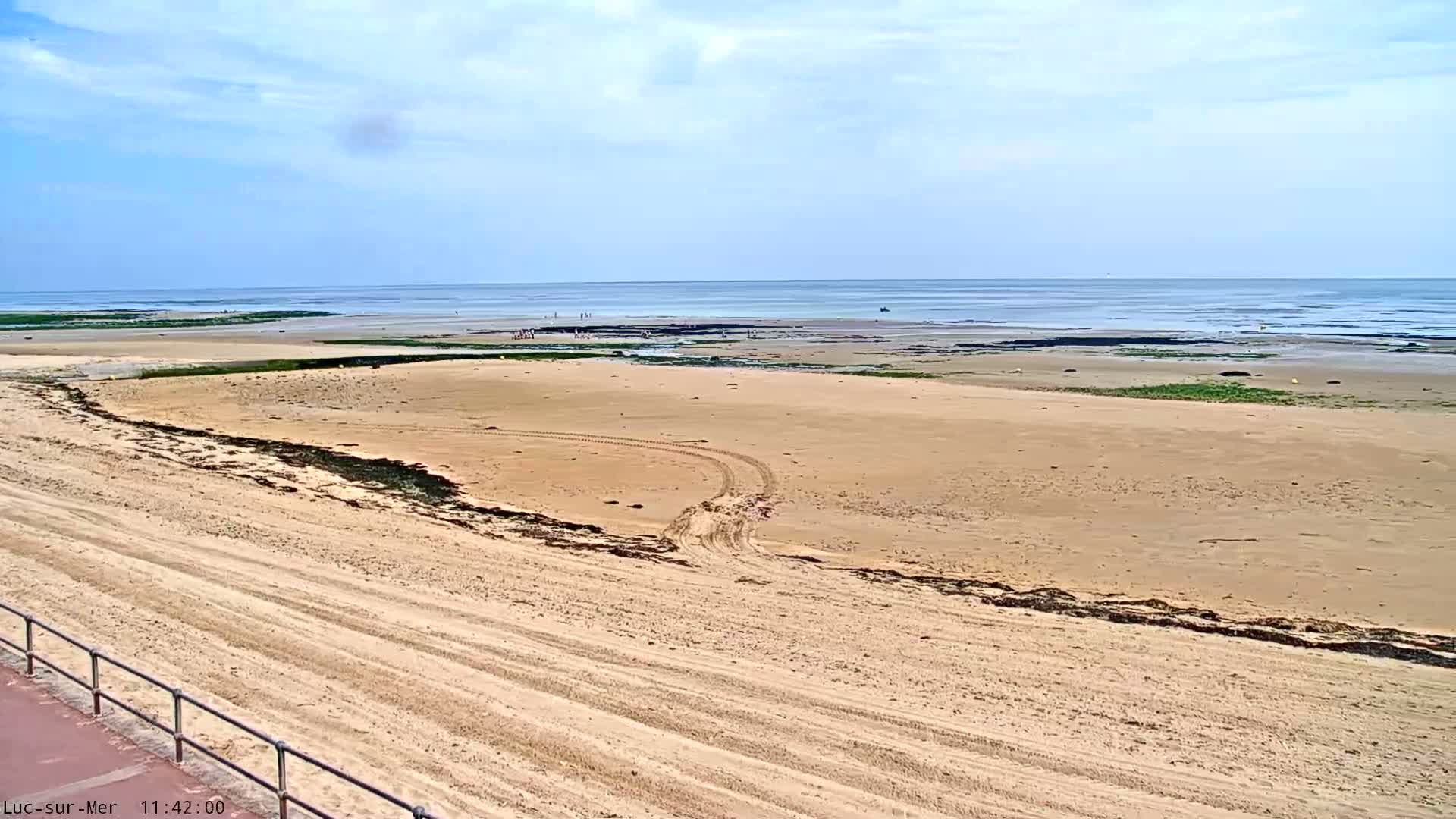A wide sandy beach stretches to a calm ocean under a mostly clear sky.