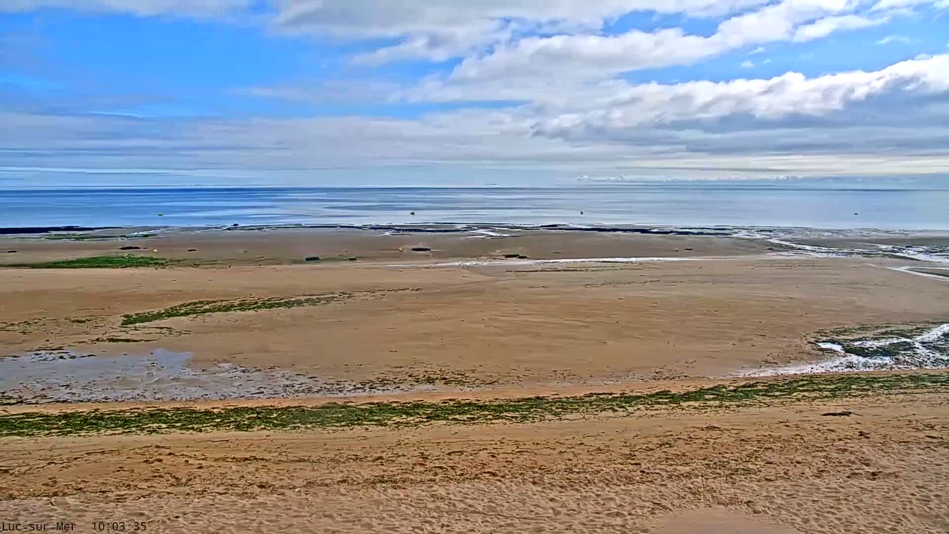A sandy beach stretches towards a calm ocean under a partly cloudy sky.
