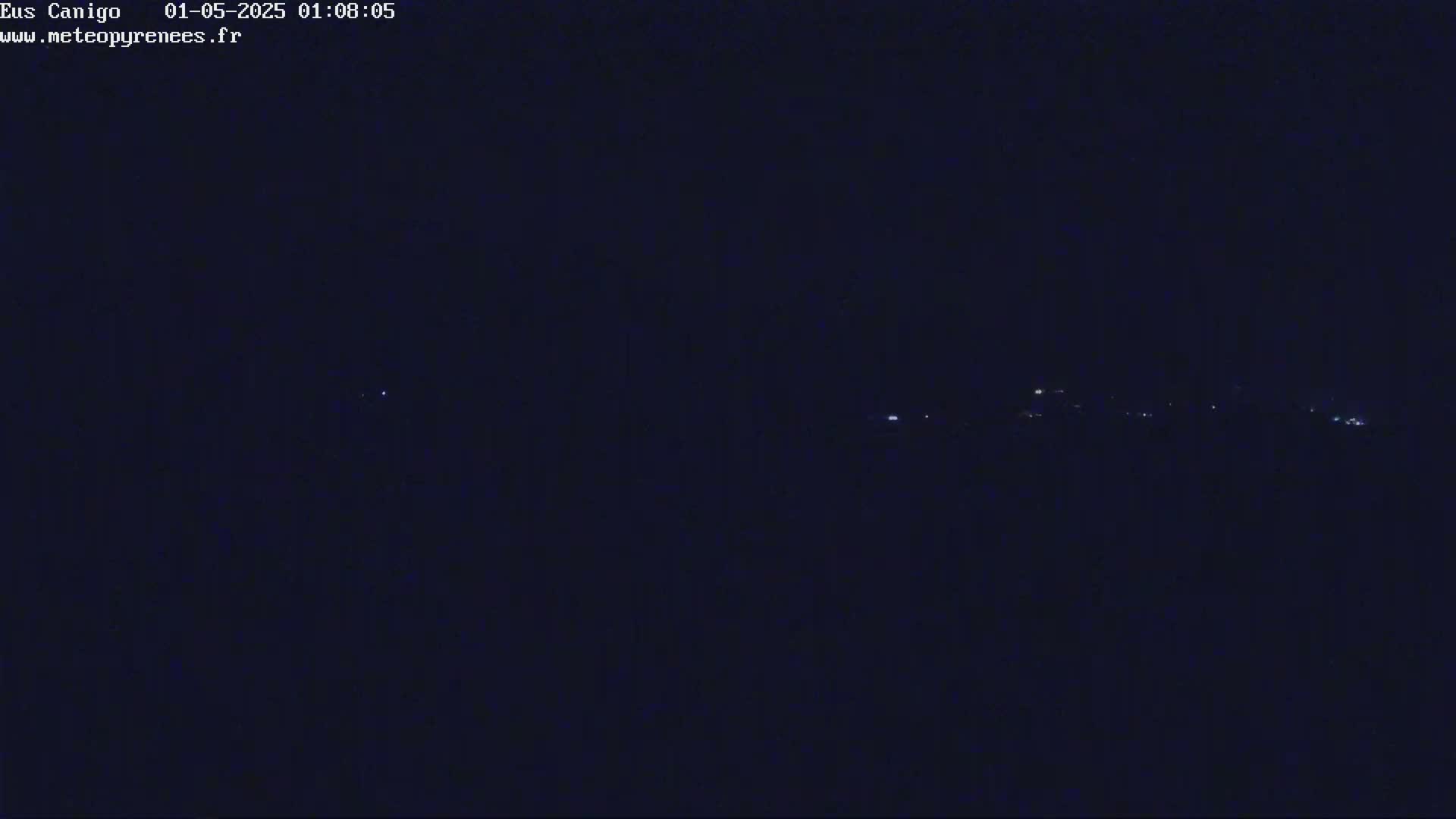 A nighttime, dark image shows a distant line of faint lights on a dark horizon.