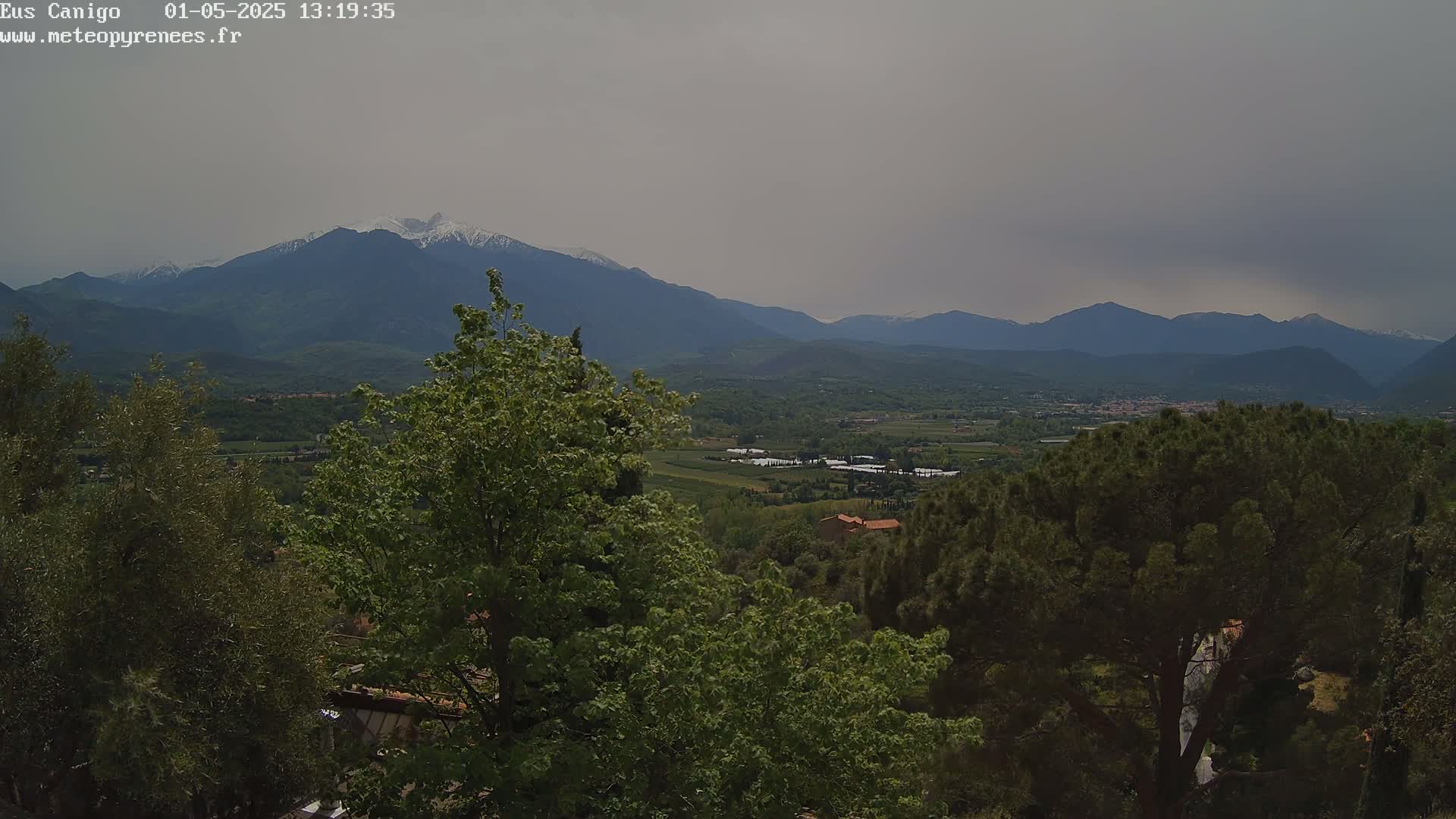 A view of a valley and snow-capped mountains under an overcast sky.