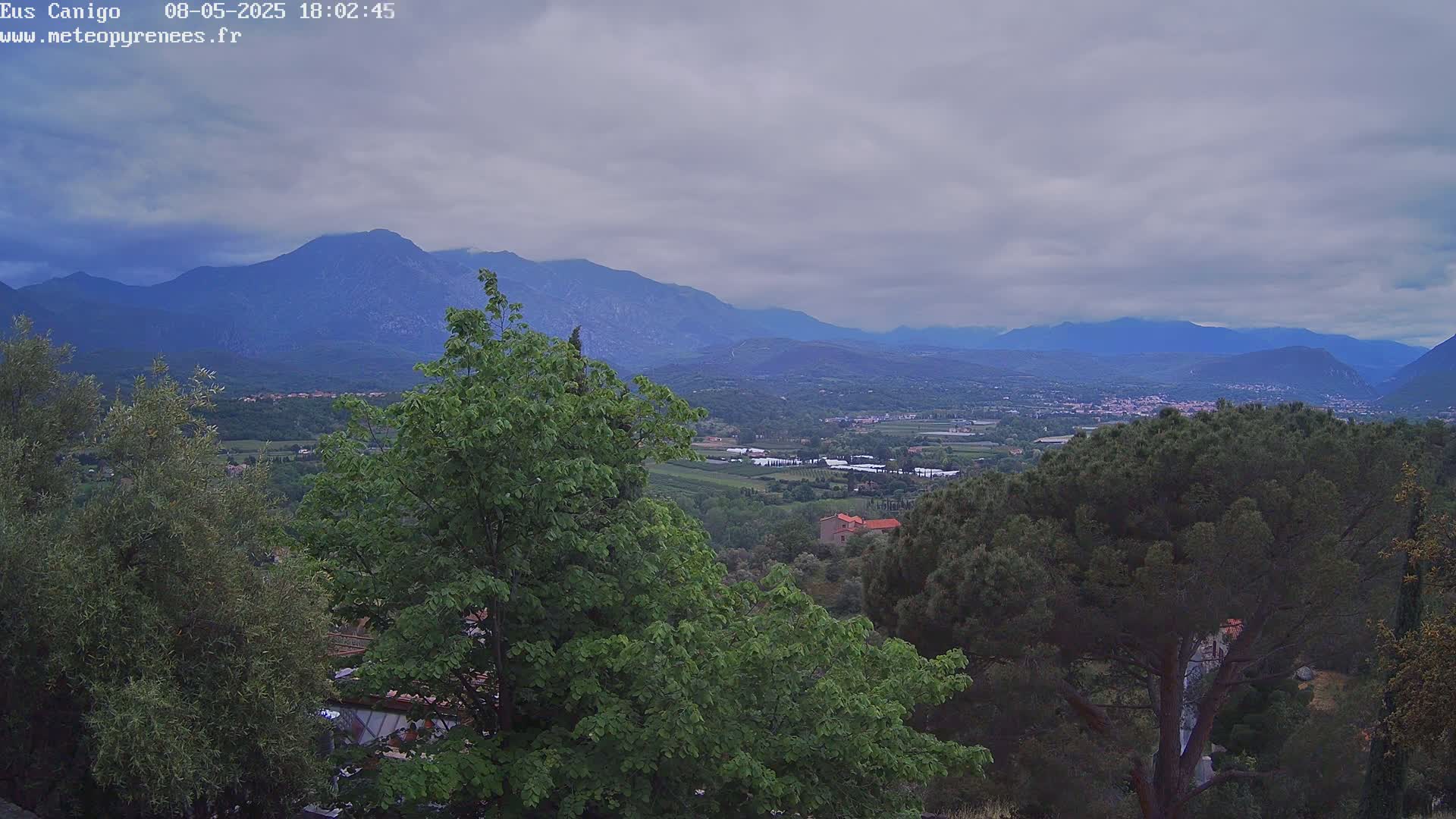 A view of a valley with green trees and distant mountains under a cloudy sky.