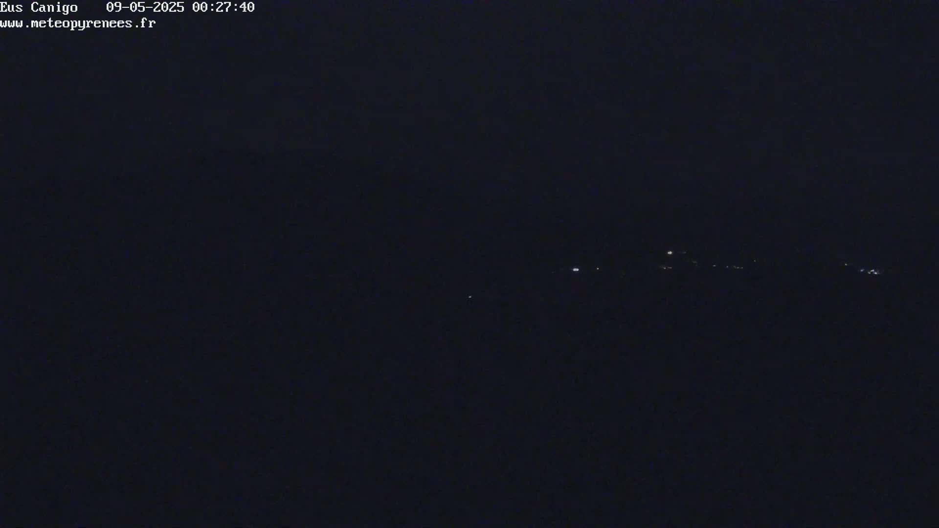 A dark, nighttime view shows a distant line of faint lights on a dark horizon.