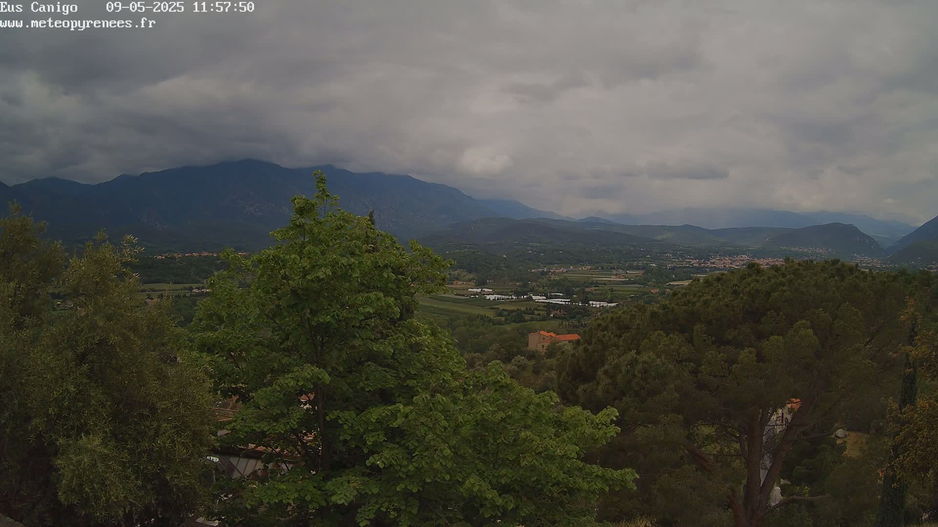 A view of a valley with green trees and distant mountains under a cloudy sky.