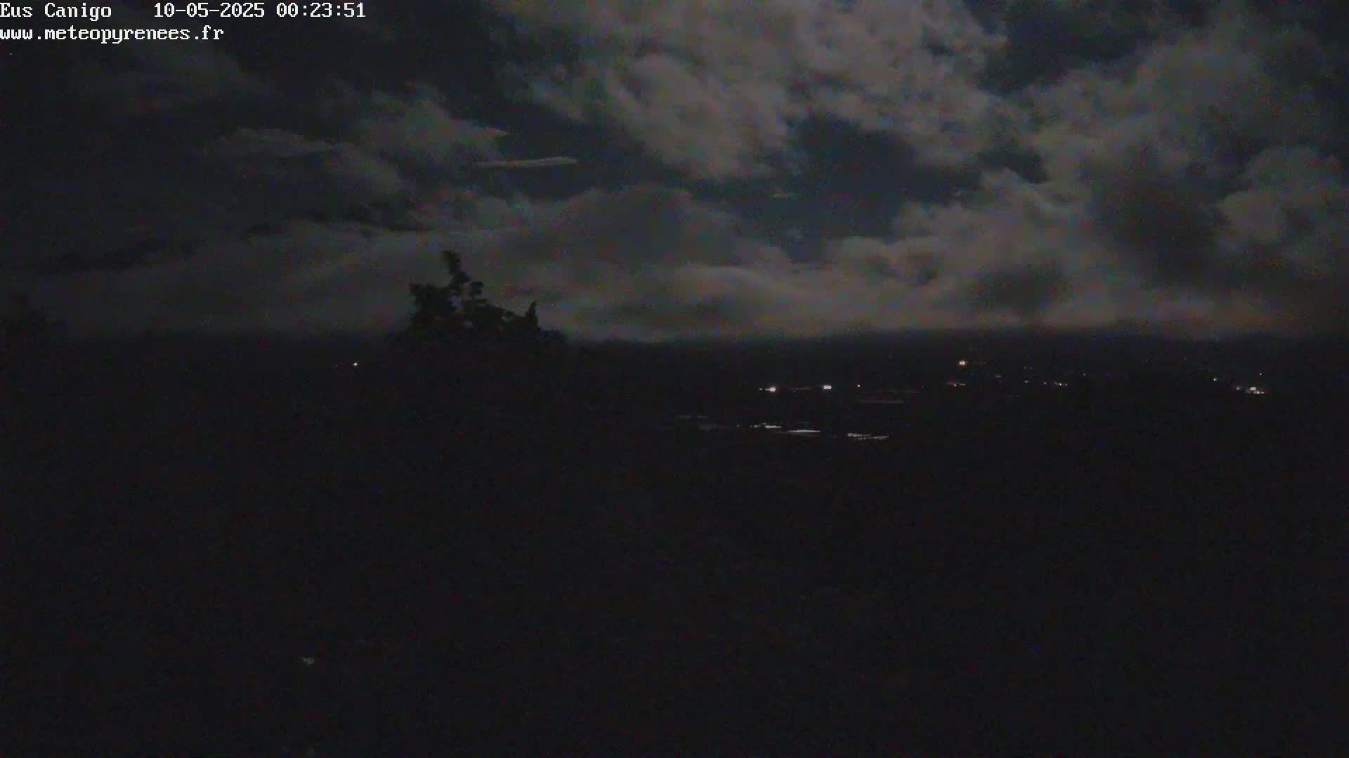 A nighttime, cloudy view of a dark landscape with a few distant lights visible.