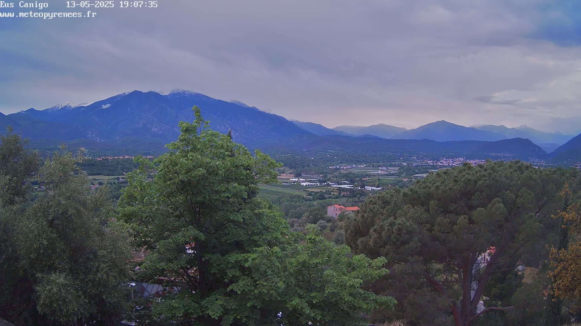 A view of a valley with lush green trees and mountains in the background under an overcast sky.