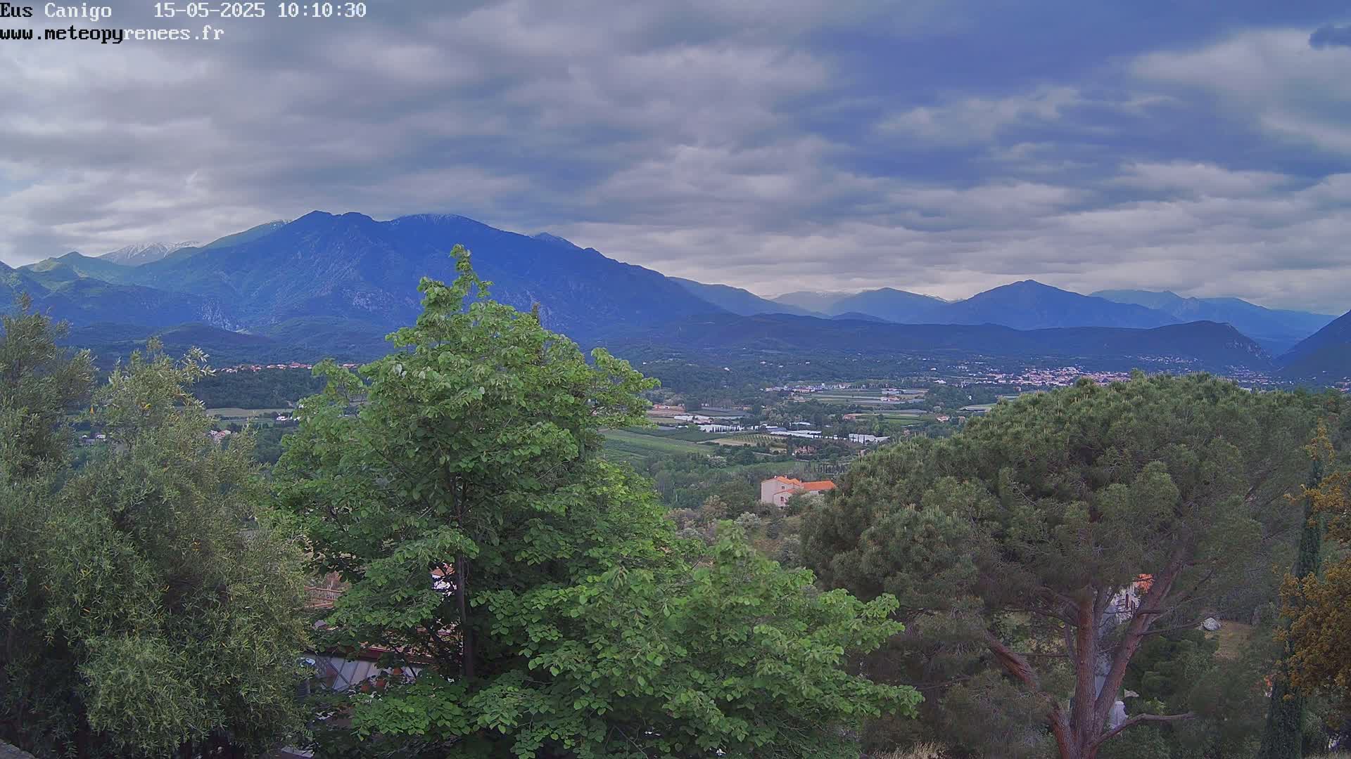 A view of a valley with green trees and distant mountains under a cloudy sky.