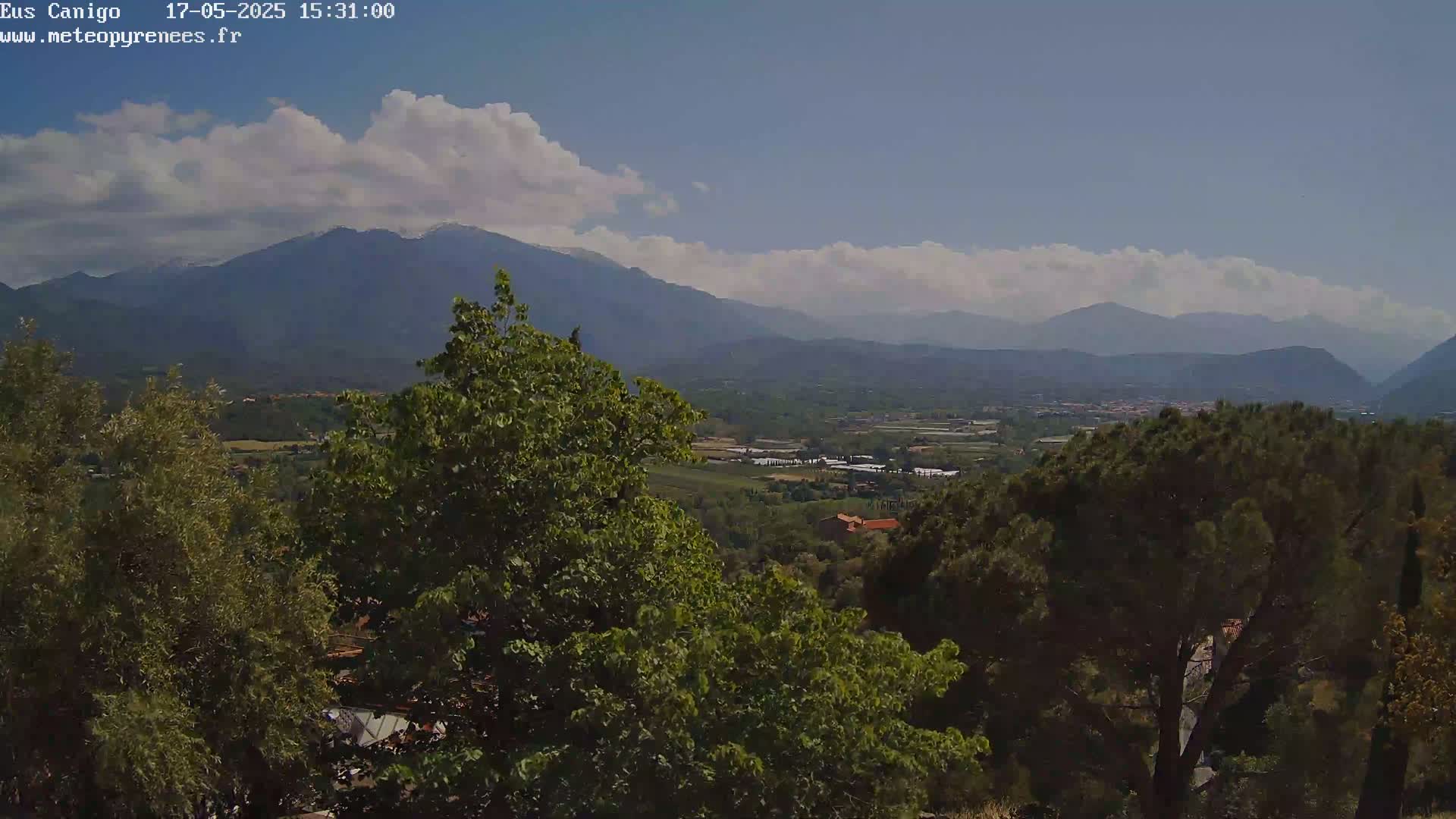 A partly cloudy sky overlooks a valley of green trees and distant mountains.