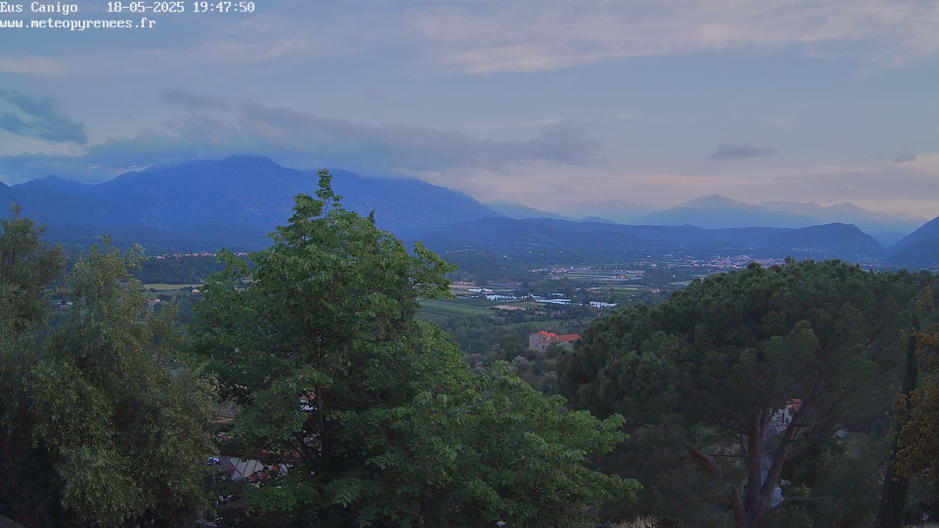 A mountain range is visible in the distance under a mostly clear, dusky sky, with green trees and a valley in the foreground.