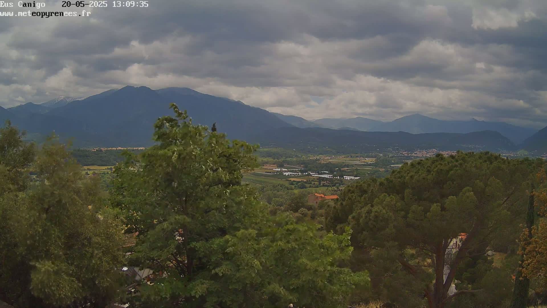 A view of a valley with green trees and mountains in the background under a cloudy sky.