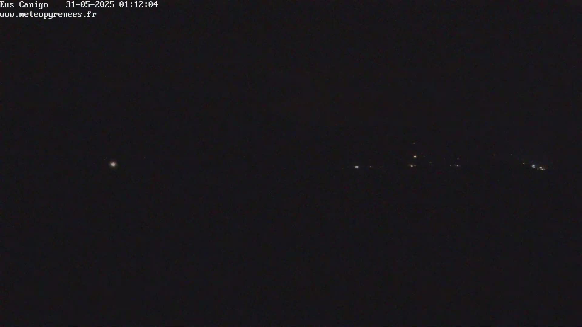 A nighttime long shot shows a dark landscape with a few faint lights in the distance under a clear, dark sky.
