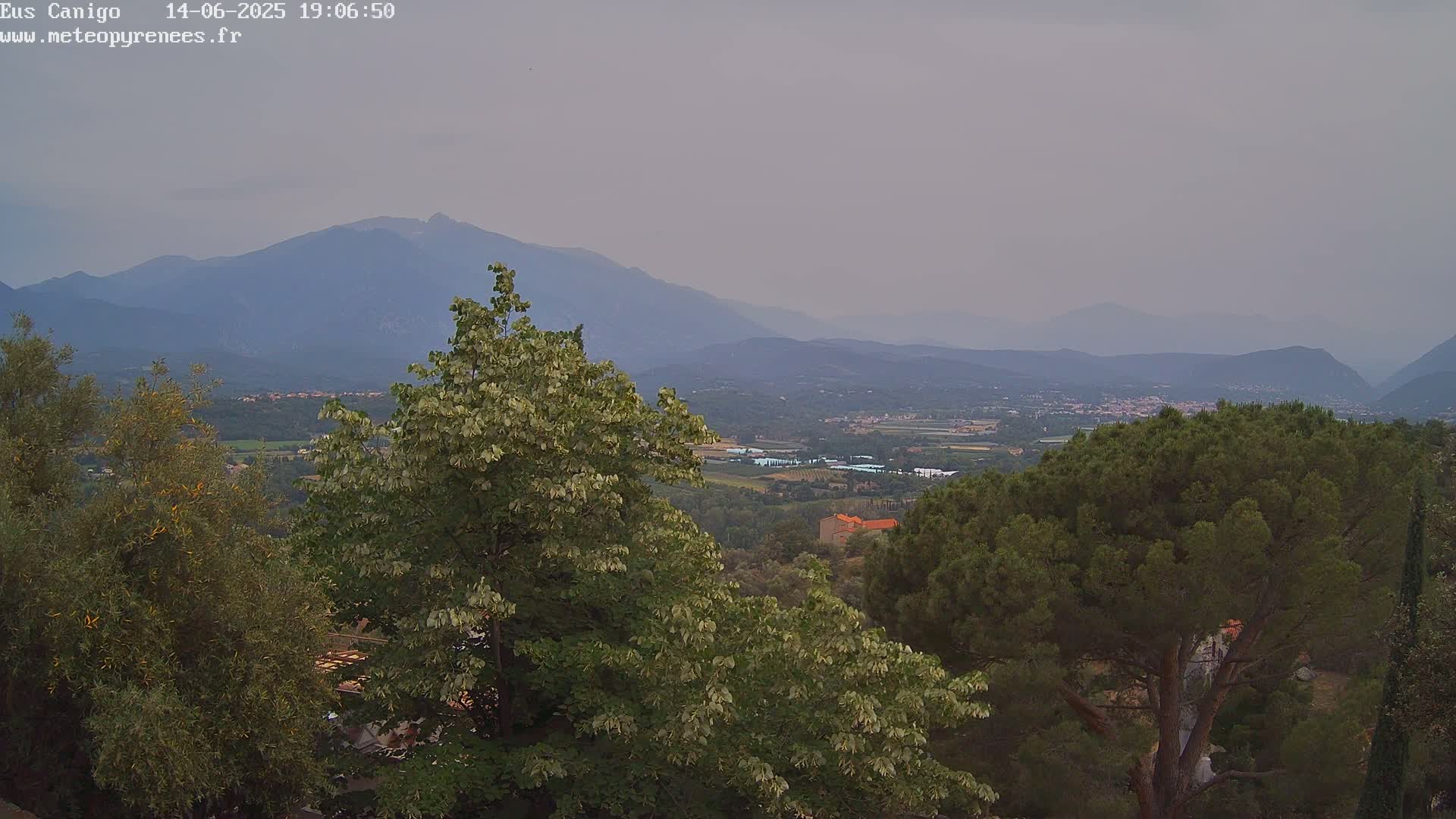A hazy, mountainous landscape is visible from a vantage point amongst green trees and shrubs.