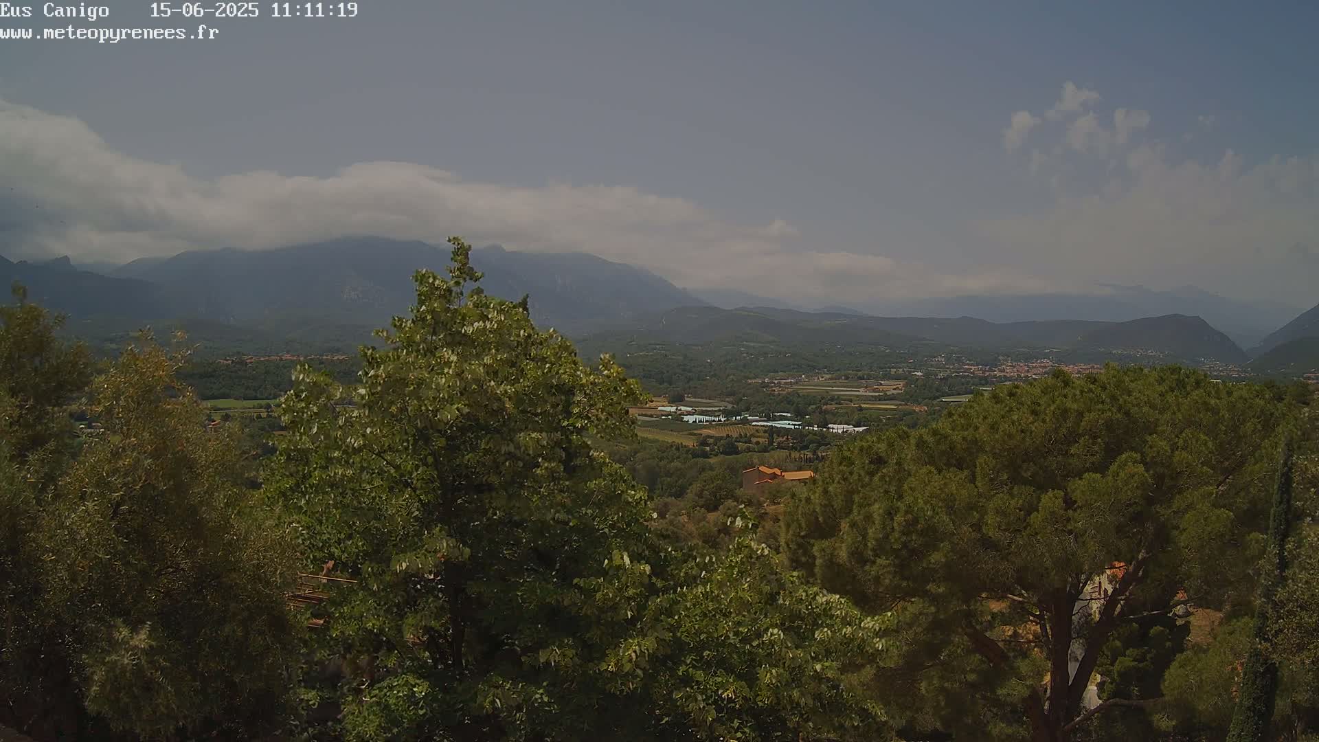 A hazy, partly cloudy day reveals a mountainous landscape with lush green vegetation, including a valley with some buildings visible in the distance.