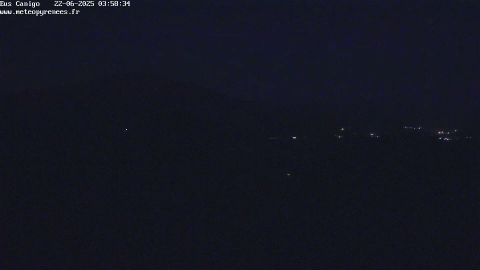 A nighttime, dark view of a mountain range with a few distant lights visible.
