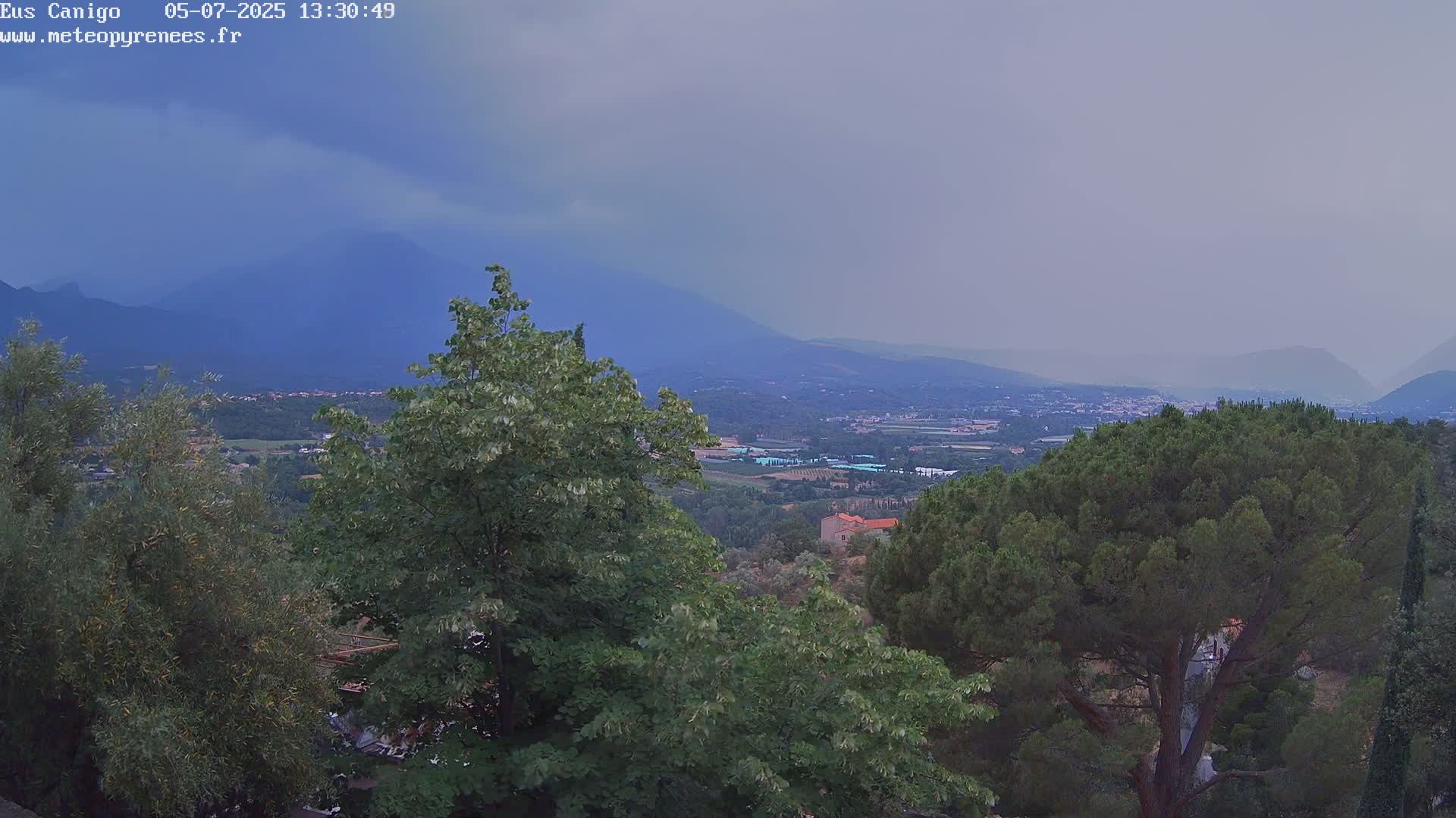 A hazy, overcast view overlooks a valley with a town nestled amongst green trees and mountains in the distance.