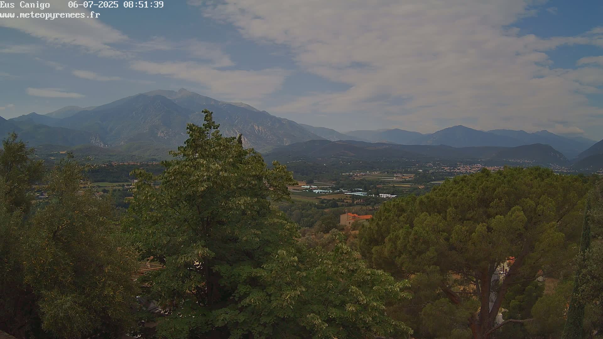 A partly cloudy sky overlooks a valley of green trees and mountains in the distance.